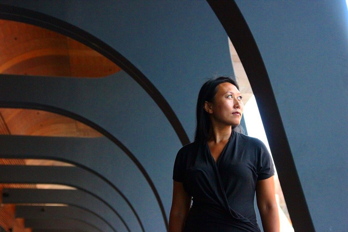 Natasha Fong beneath a run of dark architectural arches, looking towards the light